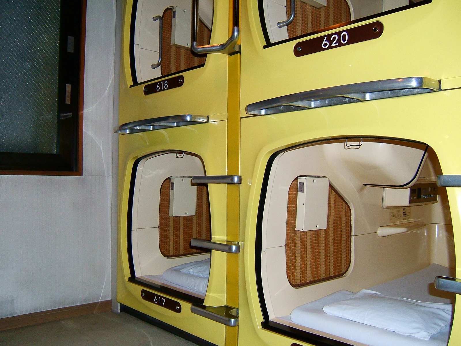 Yellow capsule pods stacked two-high inside Capsule Inn Akihabara, with sliding shutters and numbered doors