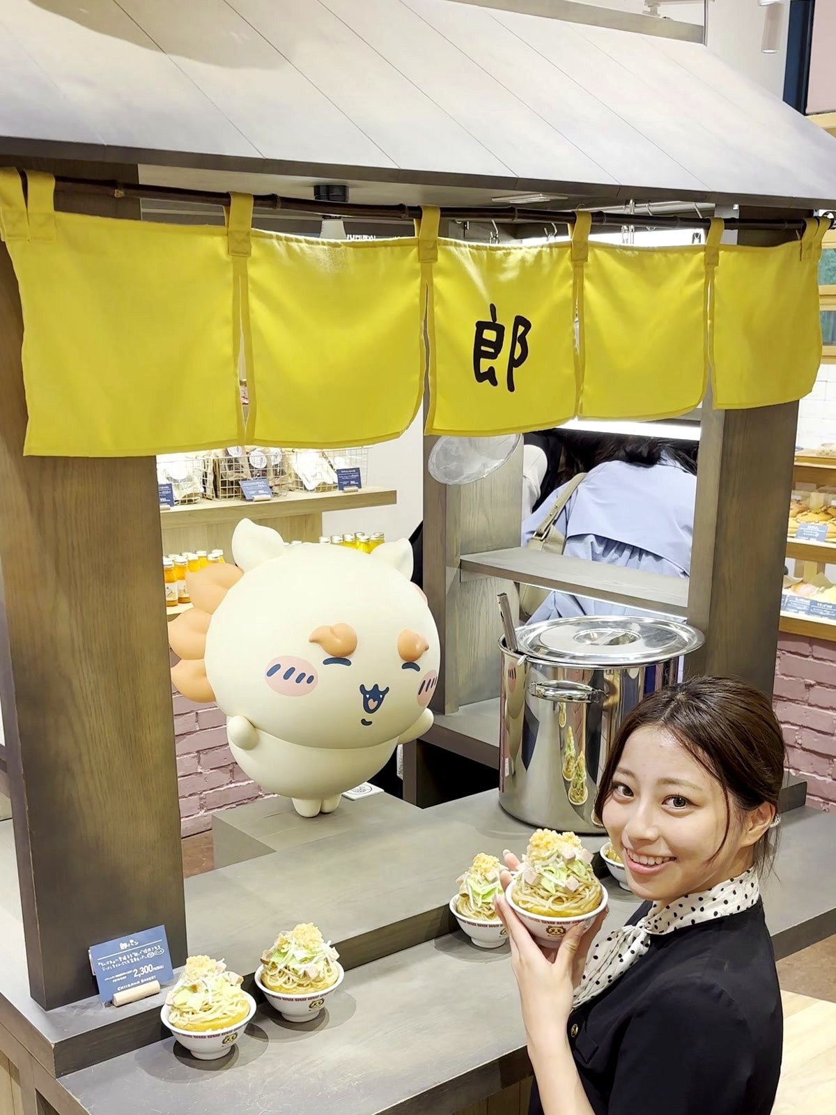 Moe from Japan Pop Now holding a matcha cupcake next to a large Chiikawa character figure at the Ro Ramen bread counter inside the bakery