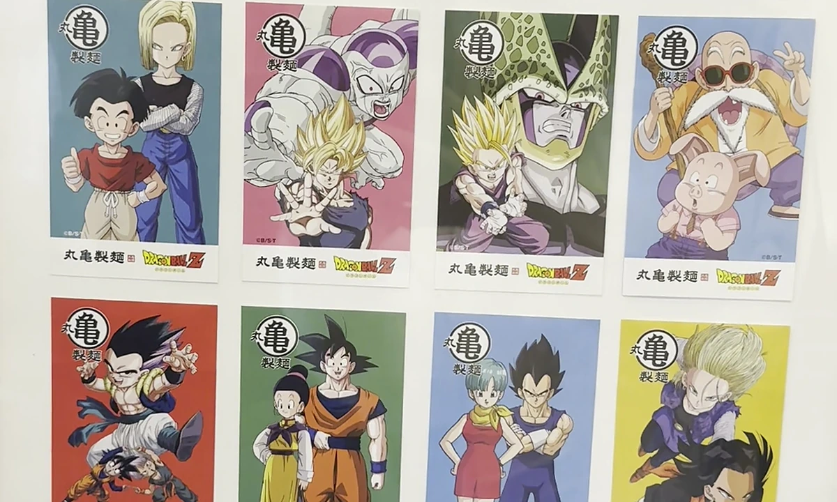 The full 16-card Phase 1 udon ticket set displayed in a plastic-window frame at the Shinjuku-Gyoen-mae pop-up — four rows of four cards, each card showing a Dragon Ball Z character above the Marugame Seimen logo with a colored background tied to the character