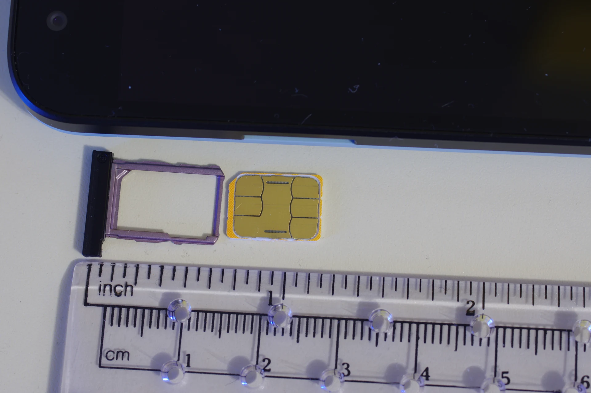 Nano SIM card next to its phone tray with a ruler showing centimeter and inch scale, the typical setup for swapping a Japan prepaid SIM into an unlocked phone