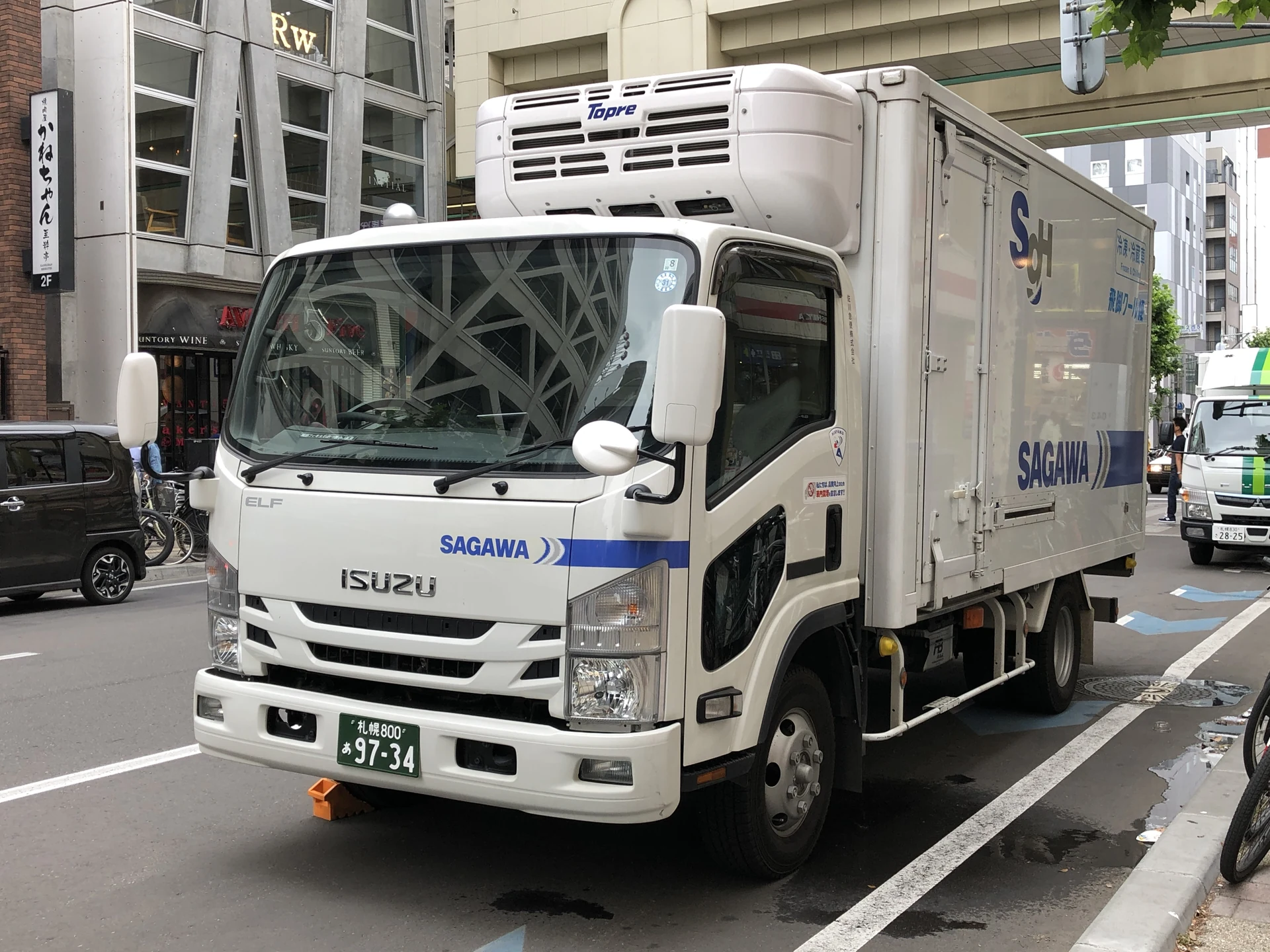 Sagawa Express Isuzu Elf delivery truck parked on a Sapporo street with the company's blue chevron livery — the same fleet used for Kansai-region takkyubin runs described below