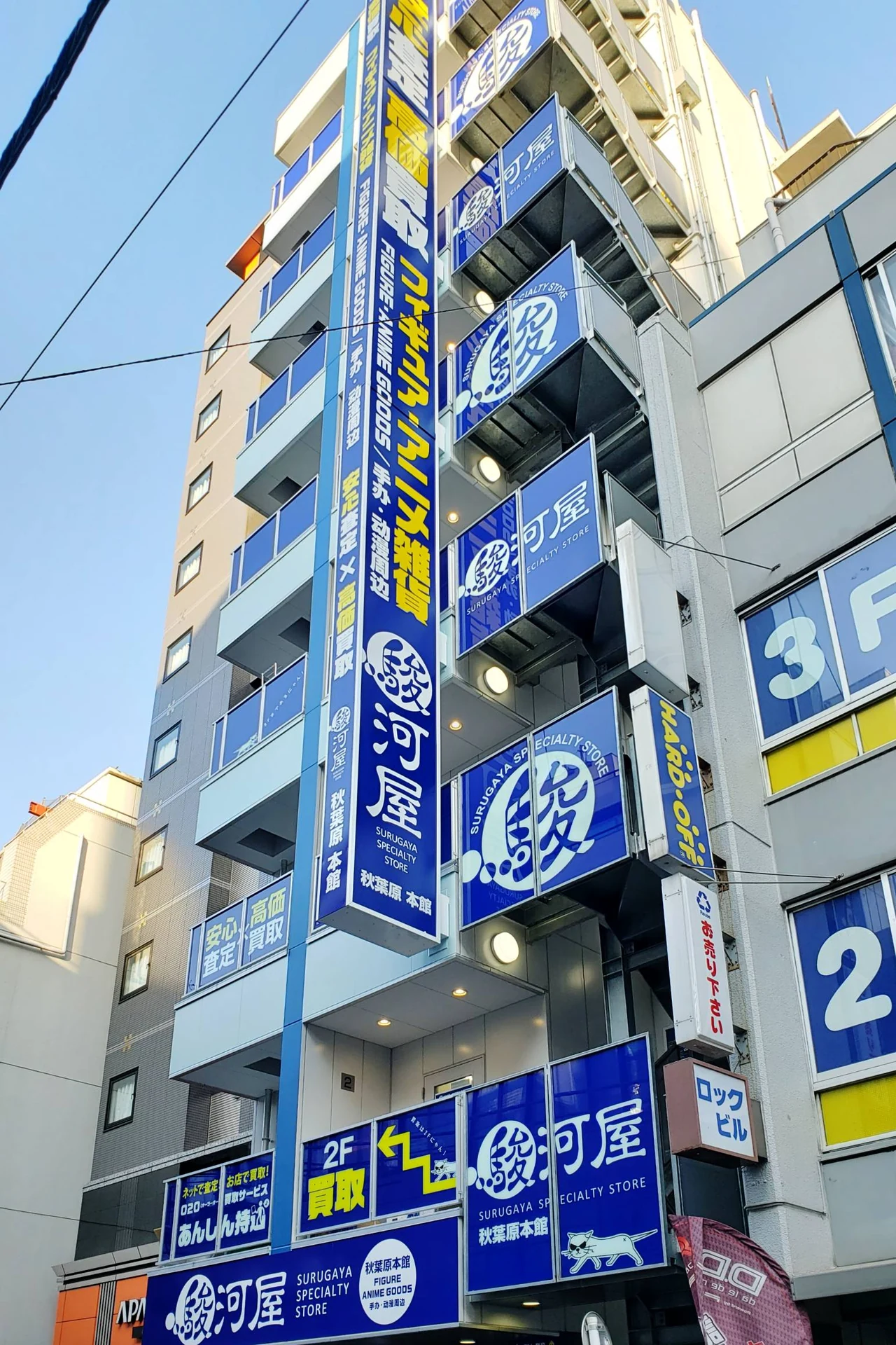 Suruga-ya Akihabara honten storefront with stacked blue floor-by-floor signage, a major Japanese second-hand chain proxy buyers source figures, games, and trading cards from