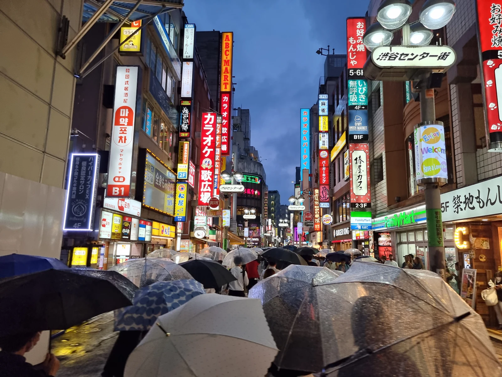 Center-Gai pedestrian street in Shibuya on a rainy afternoon, the main shopping artery of Shibuya used as a secondary arena in JJK Shibuya Incident