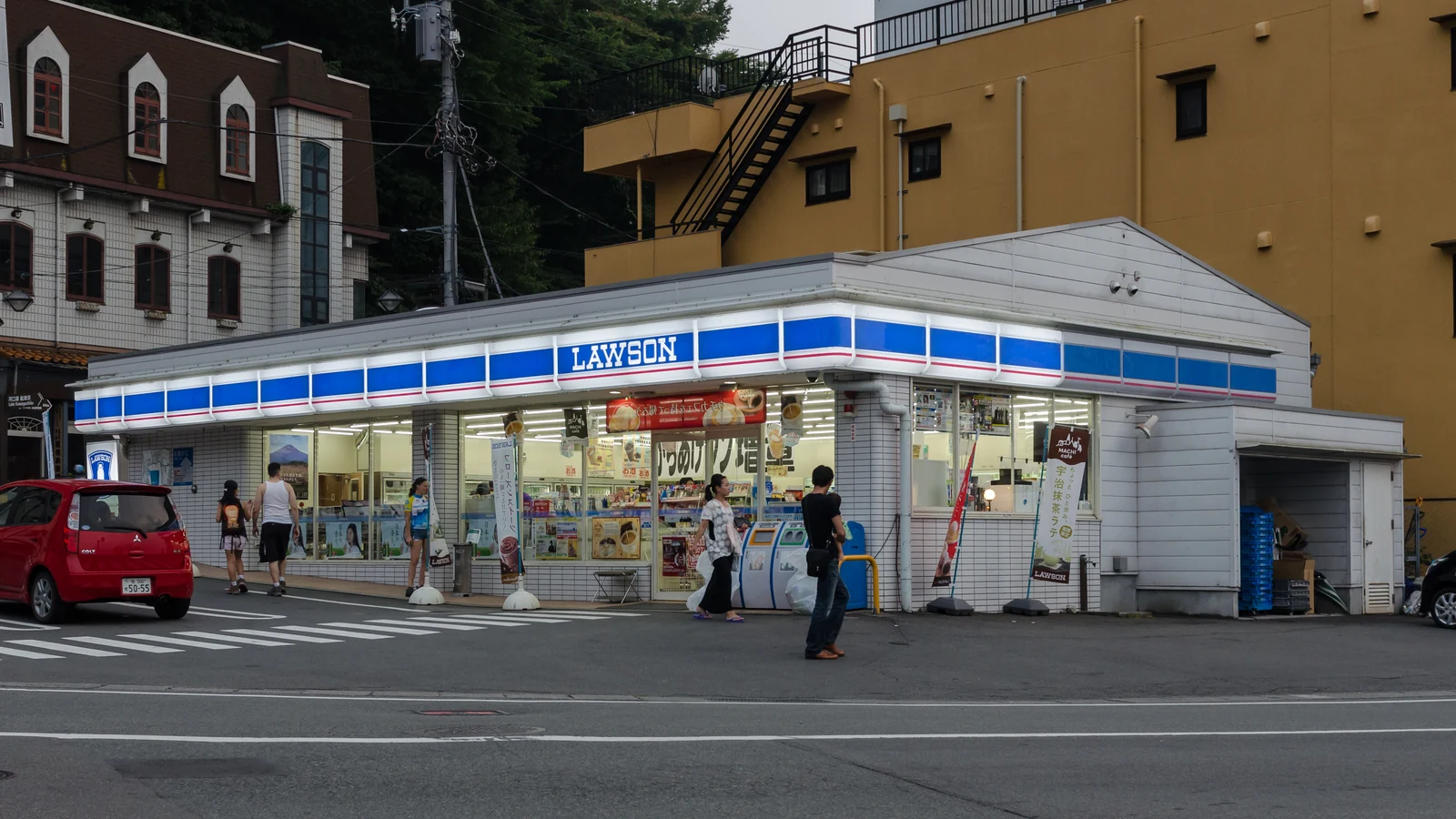 Exterior of a Lawson convenience store in Japan with the blue-and-white storefront sign anime fans walk past to reach a Loppi kiosk