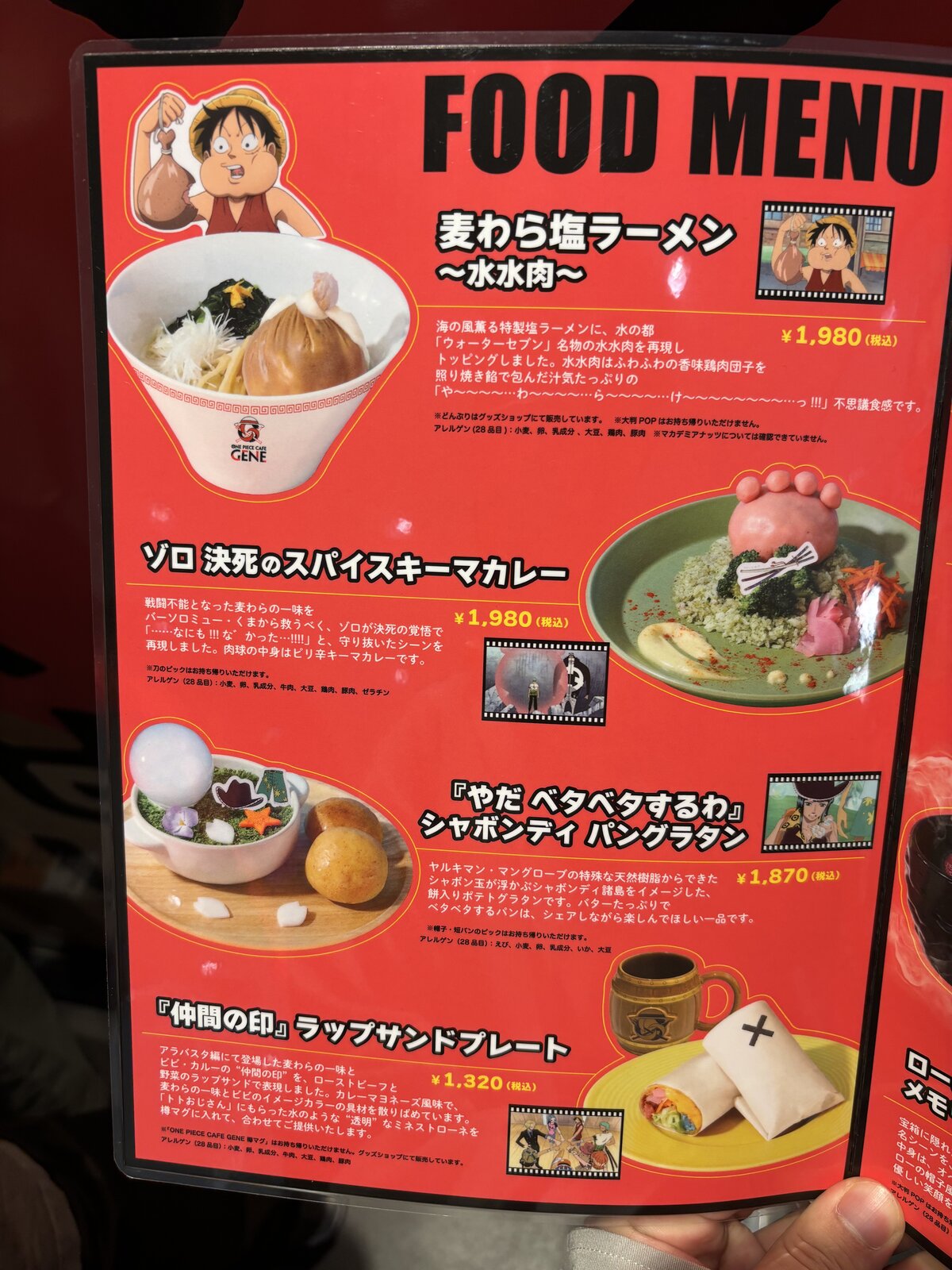 Food menu board at One Piece Cafe GENE showing Straw Hat Salt Ramen, Zoro Spicy Keema Curry, Shabondy Bread Gratin, and Nakama Wrap Sandwich Plate with prices